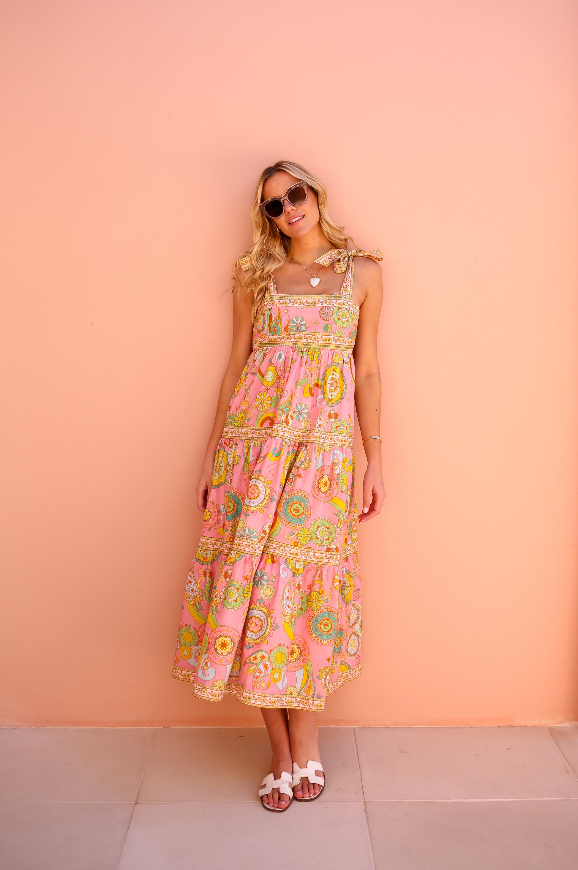 Woman wearing a colorful floral dress against a peach wall.